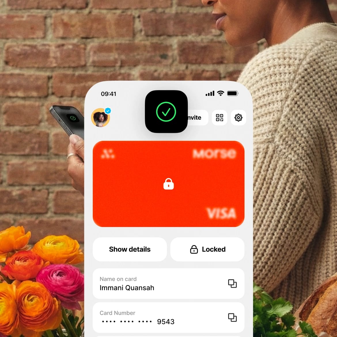 A locked Morse debit card on the app, held by a person standing by a flower stall